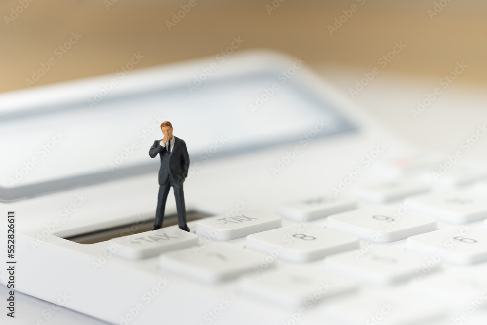 Miniature people: businessman standing on tax button of calculator. Financial, and business concept Miniature people: businessman standing on tax button of calculator. Financial, and business concept