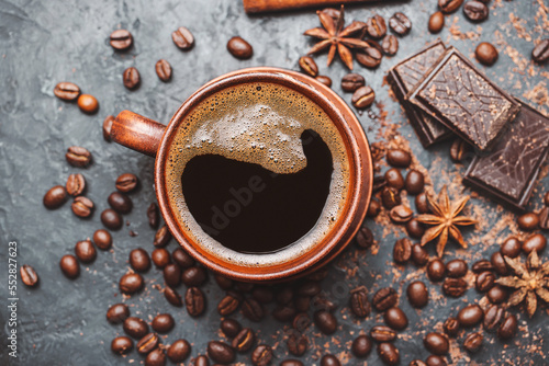Fresh brewed black coffee in a cup on dark background with coffee beans and chocolate pieces, top view © O.Farion