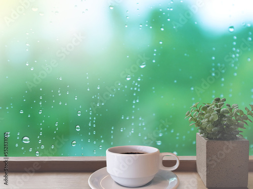 Rainy atmosphere with a drop of water on the glass. On the table there is a cup of coffee and plant pots on the wooden floor on the right. Feelings, sadness, loneliness, nostalgia.