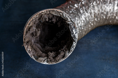 A dirty laundry flexible aluminum dryer vent duct ductwork filled with lint, dust and dirt against a blue background photo