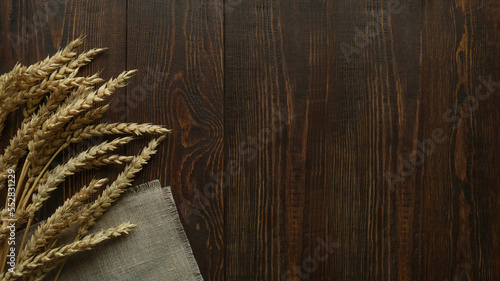 Ears of wheat and textile napkin on a dark wooden background with space for text