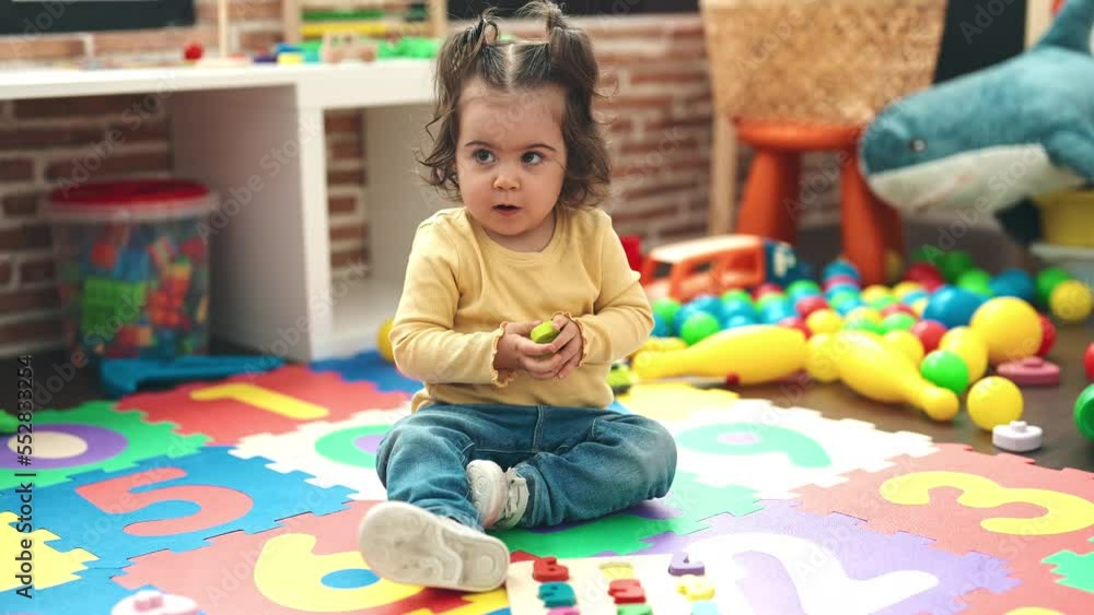 Adorable hispanic girl playing with maths puzzle game sitting on floor at kindergarten Adorable hispanic girl playing with maths puzzle game sitting on floor at kindergarten