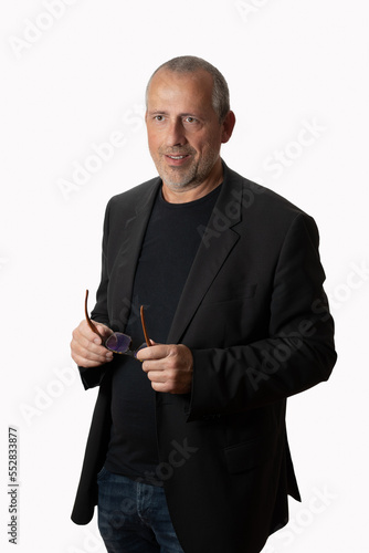 Middle-aged manager in casual suit standing before an isolated background, holding glasses, looking sidewards, smiling