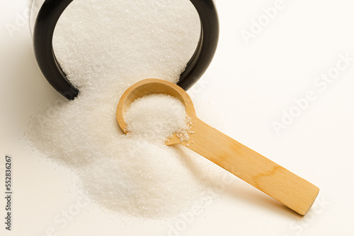 Fotografie Spilled sugar from jar and wooden spoon