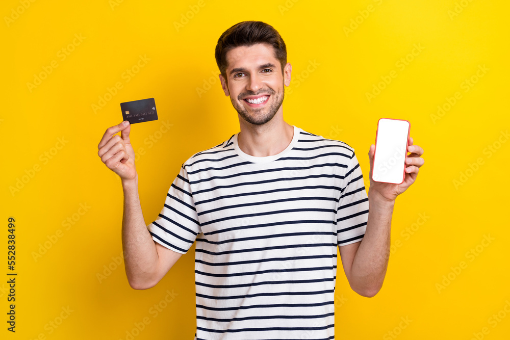 Portrait of cheerful person toothy smile hands hold debit card empty space telephone screen isolated on yellow color background Portrait of cheerful person toothy smile hands hold debit card empty space telephone screen isolated on yellow color background