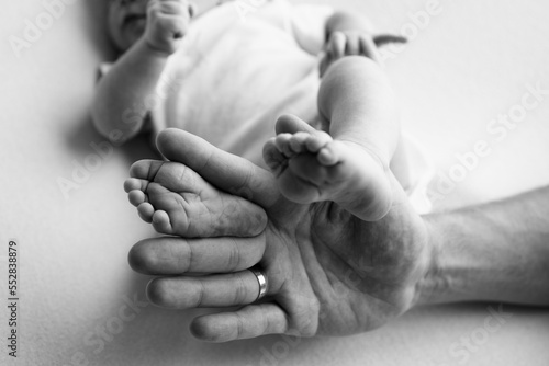 Baby feet in the hands of mother, father, older brother or sister, family. Feet of a tiny newborn close up. Little children's feet surrounded by the palms of the family. Black and white.
