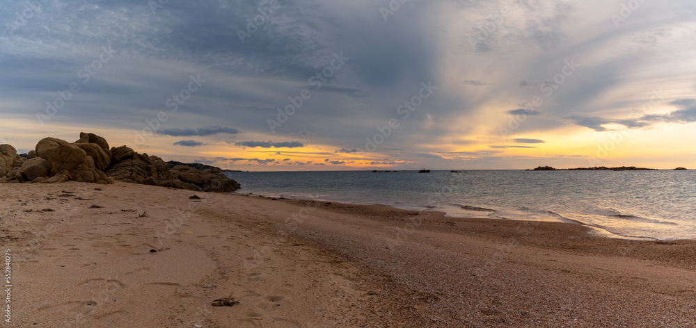panorama view of a golden sand beach at sunset with calm ocean water and red granite rocks