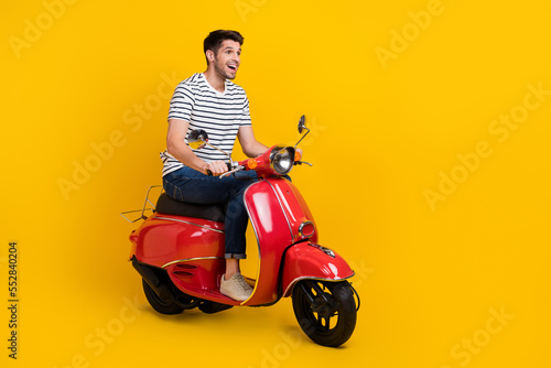 Full length photo of carefree excited man wear white t-shirt driving bike looking empty space isolated yellow color background © deagreez
