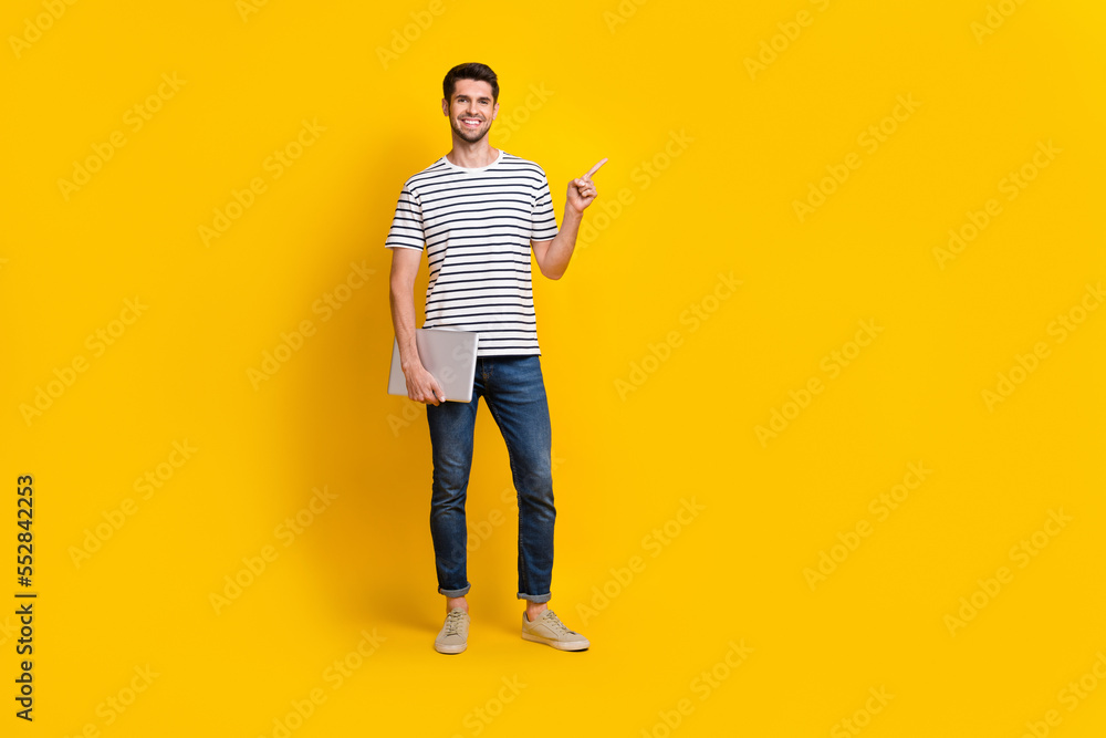 Fototapeta premium Full length photo of sweet charming man wear white t-shirt holding modern gadget pointing empty space isolated yellow color background