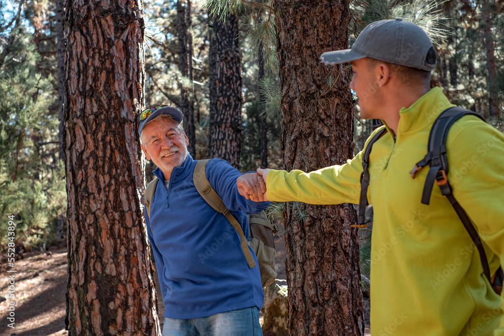 Senior grandfather and young grandson hiking together in the woods sharing the same passion for nature and healthy lifestyle. Boy of new generation help the old one to stay fit