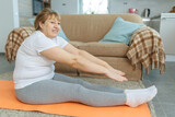 Overweight mature woman doing abs exercise on yoga mat at home