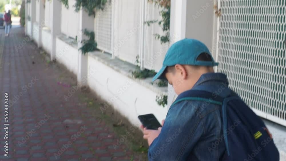 A teens hand holds a smartphone with an online map app marked with a destination. In the background is a city street. Concept of Internet navigation and modern technology. boy tourist walks A teens hand holds a smartphone with an online map app marked with a destination. In the background is a city street. Concept of Internet navigation and modern technology. boy tourist walks