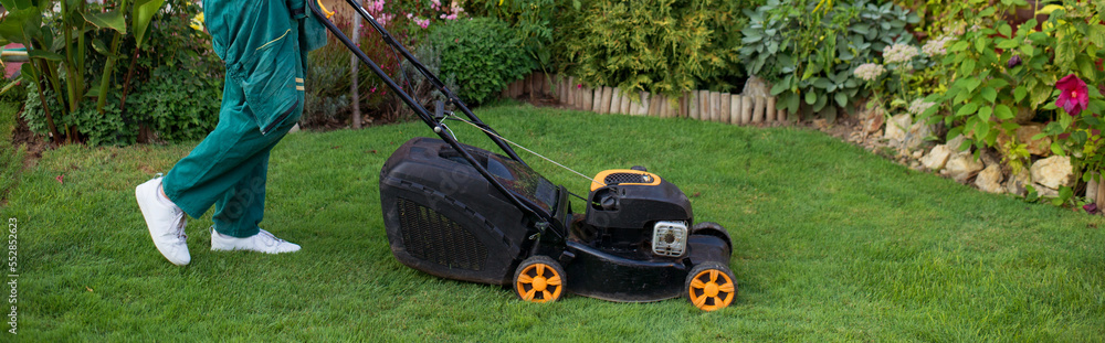 Fototapeta premium Young gardener mowing the lawn with lawnmower in summer