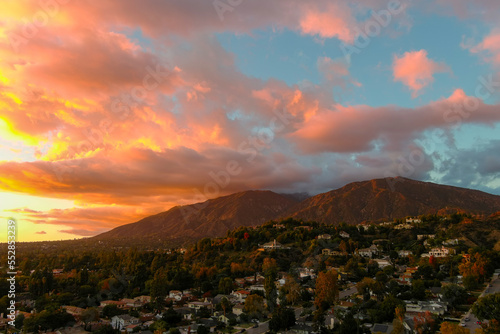 aerial shot of majestic mountains with powerful clouds and blue sky with homes, apartments and lush green trees at sunset in Monrovia California USA photo