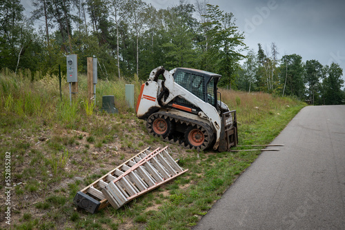 Obraz na płótnie Mini front end loader with forklift attachment parked next to a paved street with two ladders, at a new home construction site. w salonie