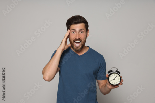 Fotografía Emotional bearded man with alarm clock on light grey background