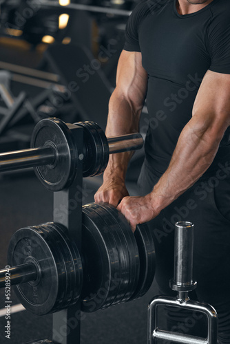 Muscular strong arms of bodybuilder. Barbells plates. Muscular man trains strong arms. Camera focus on the hands. Barbell workout