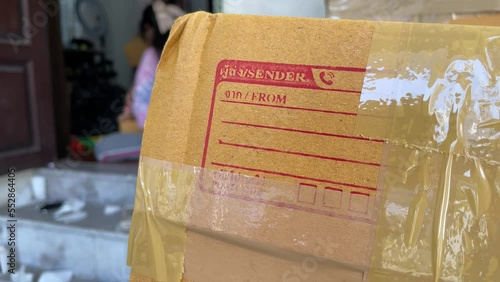 Close up cardboard box package with sender and postcode word screen on parcel with blurred person working in background
