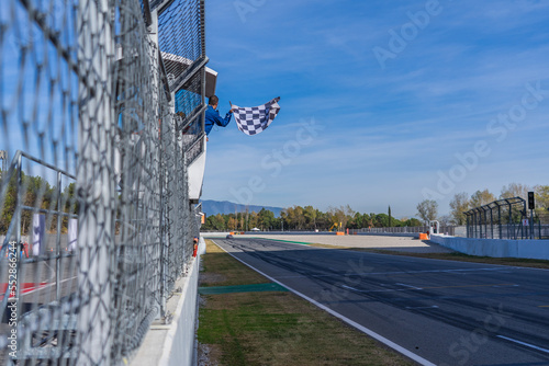 Man holding and waving checkered race flag at the finish line on a race track. Victory, achievement, success and sport concept.