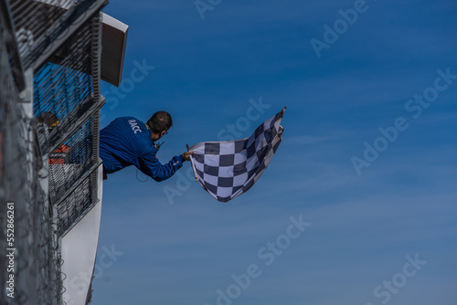 Man holding and waving checkered race flag at the finish line on a race track. Victory, achievement, success and sport concept.
