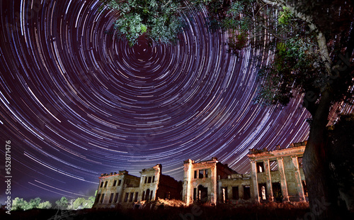 Star trails in night sky with an old abandoned ruined castle on a foreground. Glowing startrails time in night sky through the windows of the building of wolf man Pankeev