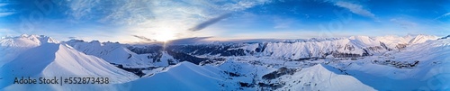 Wide aerial panorama of snowy mountain ridge on winter sunrise. Stunning mountains range covered with snow powder on ski resort at sunset. Caucasus mountain peaks skyline in Georgia - Gudauri.