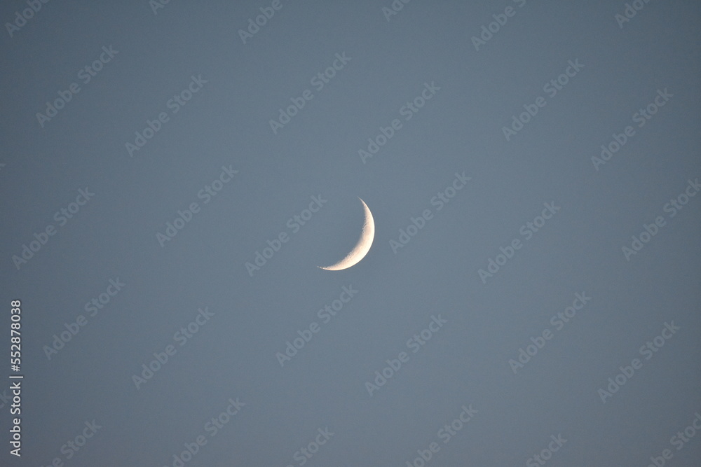 Waxing Cresent moon early on a clear evening backdropped against a light blue sky. Craters visible on surface. Waxing Cresent moon early on a clear evening backdropped against a light blue sky. Craters visible on surface.