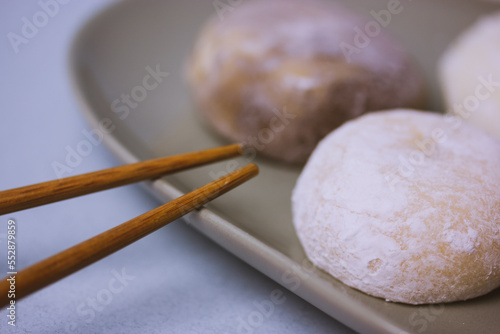 Chopsticks and traditional Japanese dessert mochi or daifuku in rice dough close-up. Four mochi ice cream balls on gray plate on blue-violet table selective focus. Asian sweet delicious food dessert.