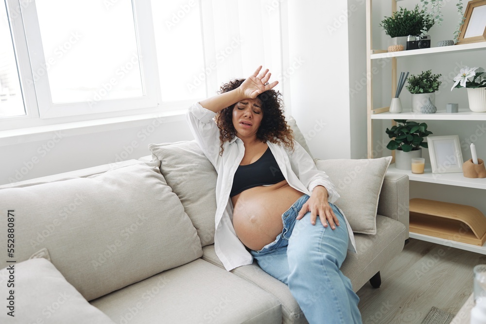 Pregnant woman headache lies at home on the couch fatigue and heaviness in the last month of pregnancy before childbirth, motherhood difficulties Pregnant woman headache lies at home on the couch fatigue and heaviness in the last month of pregnancy before childbirth, motherhood difficulties