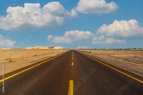 View to the long straight road and blue sky with white clouds over horizon. Amazing outdoor journey during bright summer day.