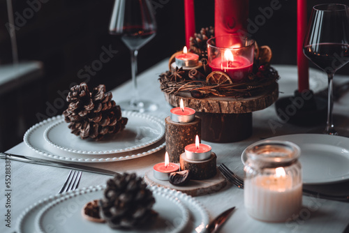 Rustic table decor for Christmas or New Year family dinner. Centrepiece with red candle  dry orange  cone  cinnamon  anise. Zero waste eco-friendly home. Cozy atmosphere  dark background. Close up