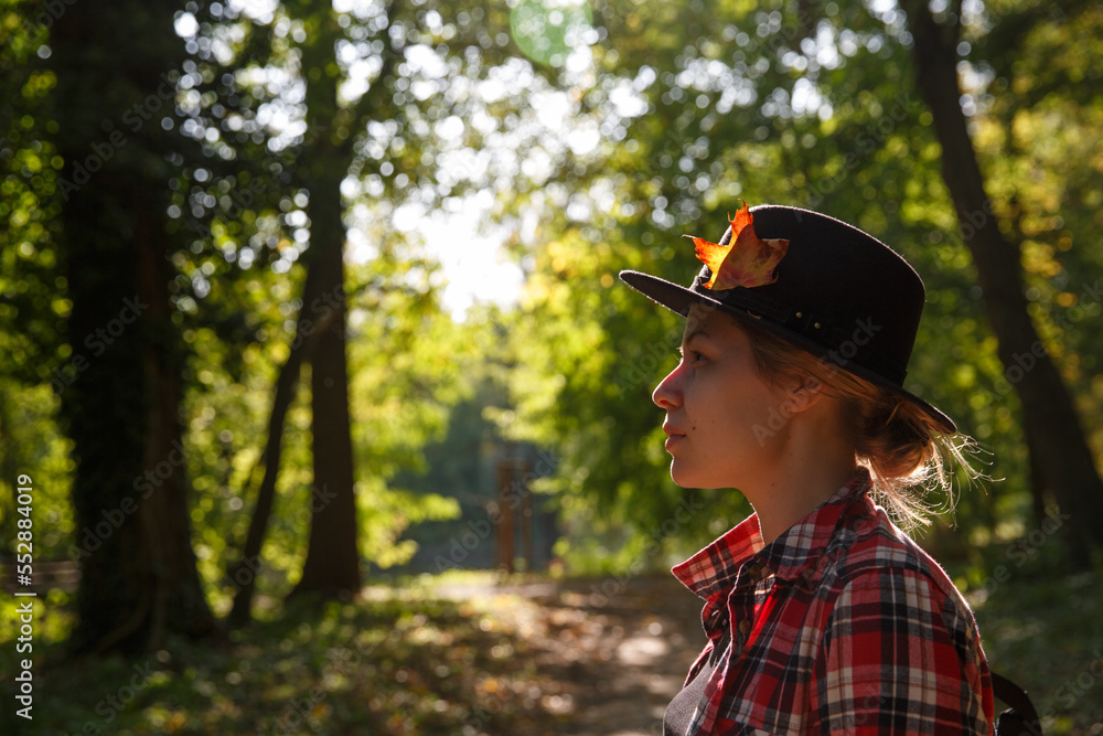 a young girl in a felt hat stands and plaid shirt in the park in the sun. selective focus