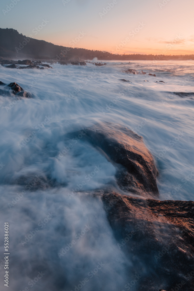 sunset at the beach with ocean waves crashing into rocks