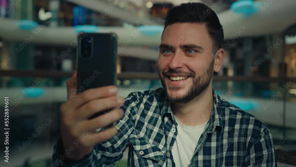 Smiling arabian caucasian male blogger businessman look at mobile phone camera talk video call in shopping mall happy young man chatting online recording blog use modern tech for remote communication Smiling arabian caucasian male blogger businessman look at mobile phone camera talk video call in shopping mall happy young man chatting online recording blog use modern tech for remote communication