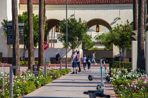 people standing in front of Union Station train station with electric scooters, colorful flowers and lush green palm trees and plants in Los Angeles California USA