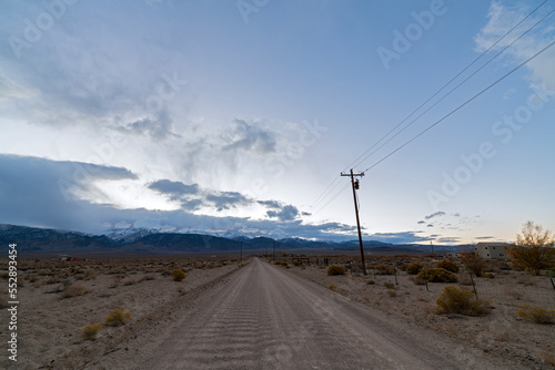 A dirt road leads to snow-capped mountains at sunset in the desert of western Nevada, USA
