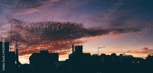 A dramatic evening sunset creates an atmospheric sky in shades of blue, violet and orange, and on the foreground, a horizontal sequence of residential buildings silhouettes with their TV antennas