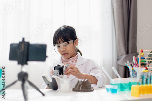 Asian school girl making easy chemistry experiments and recording a video for his followers, Young blogger kid posing in front of camera for vlog, Children make vlog for social media channel concept.