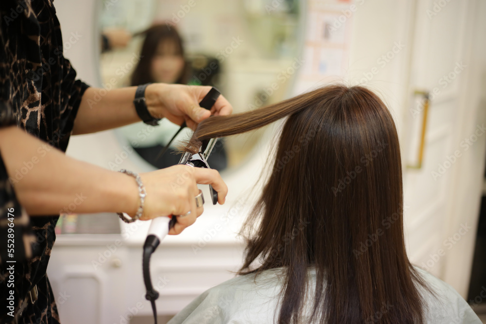 女性の髪にヘアアイロンをかける男性美容師 女性の髪にヘアアイロンをかける男性美容師