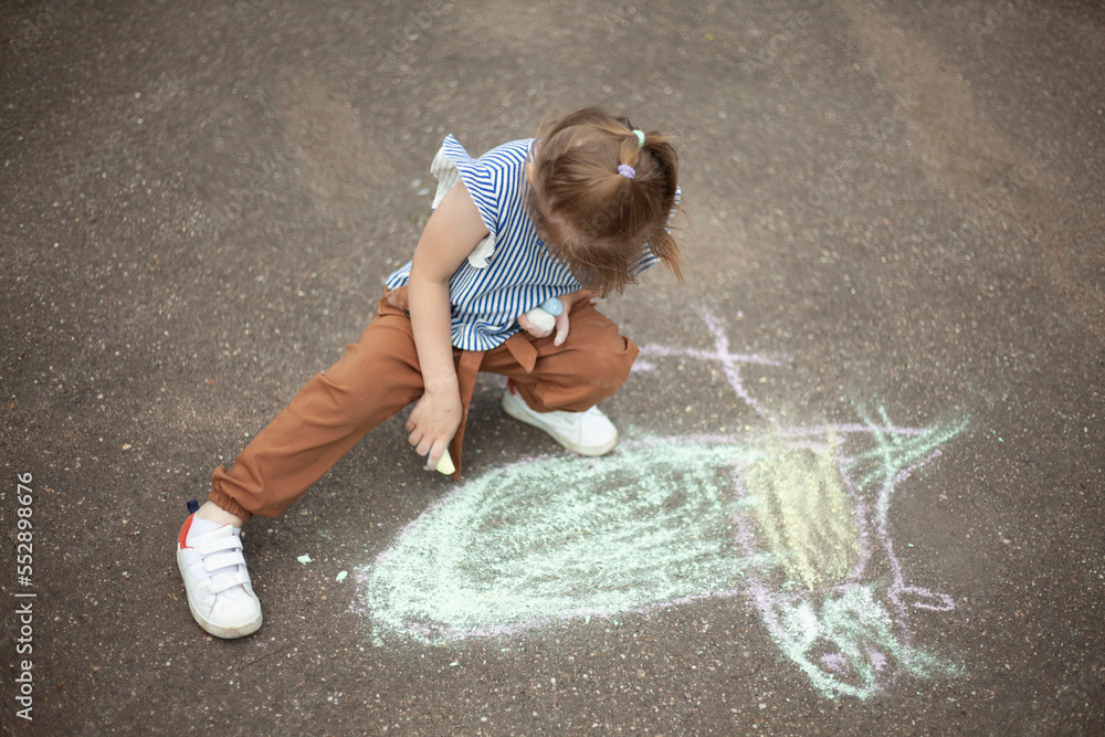 Naklejka premium Child draws on asphalt with chalk. Child plays outside. Creative abilities of baby.