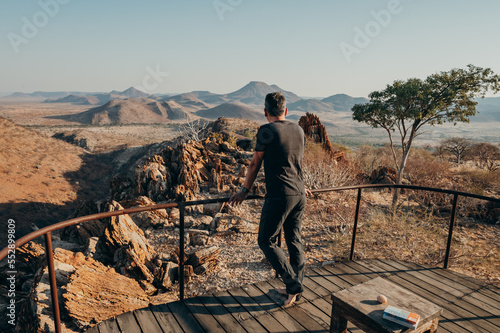 Frau schaut von einem Veranda in die weite Berglandschaft im Kaokoveld, Etambura, Namibia photo