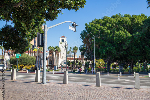 Union Station train station surrounded by office buildings, parked cars, tall lush green palm trees and plants and people walking on the sidewalk with a clear blue sky in Los Angeles California USA photo