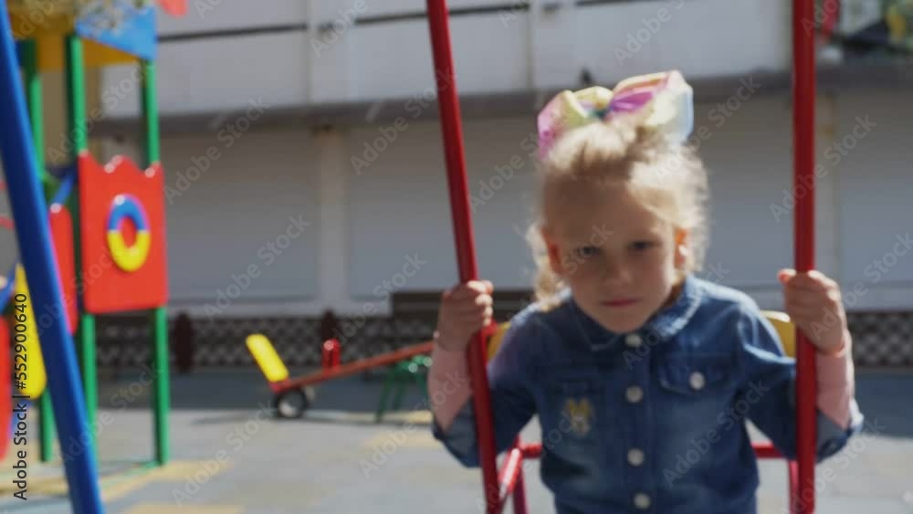 childhood, games-little blonde girl plays on the swing looking at the camera childhood, games-little blonde girl plays on the swing looking at the camera