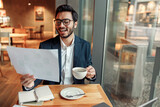 Smiling indian businessman drinking coffee and working with documents in cafe