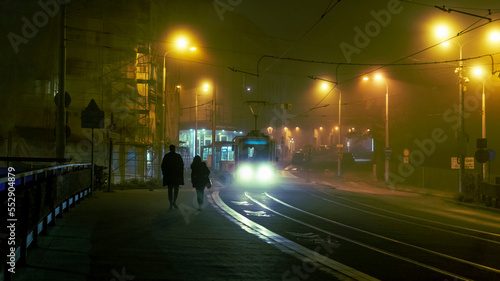 Photography Foggy town with tram and pedestrians with ambient street lights