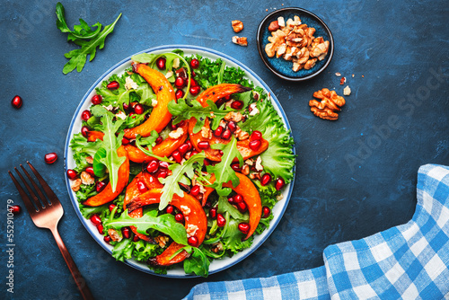 Healthy eating pumpkin salad with baked sweet pumpkin, lettuce, arugula, pomegranate seeds and nuts. Comfort food. Blue background. Top view