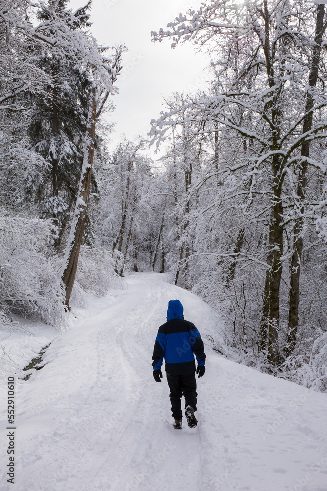 A male outdoor enthusiast walks down a snowy trail surrounded by snow-covered trees in winter
