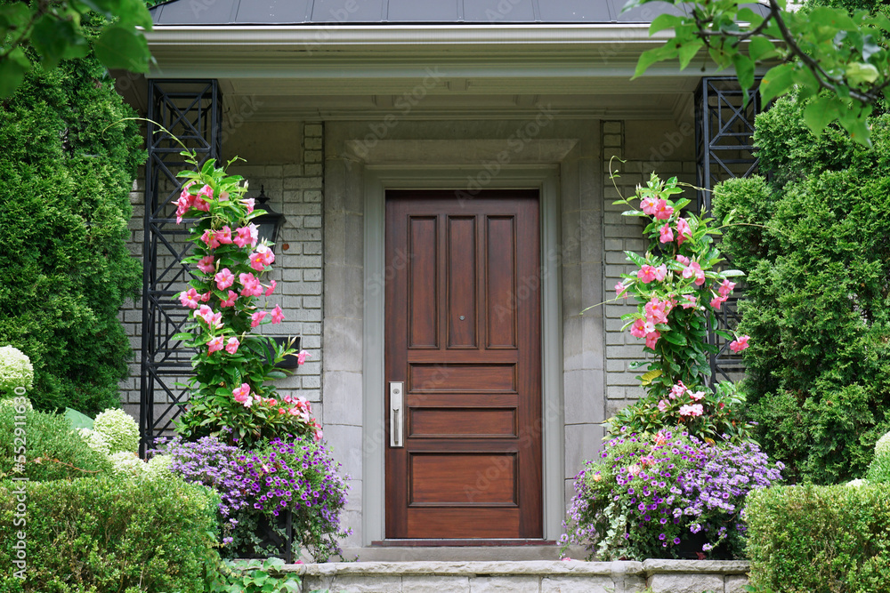 Modern style wood grain front door of house, surrounded by bushes and flowers Modern style wood grain front door of house, surrounded by bushes and flowers