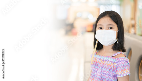 Asian child or kid girl wearing white face mask to close mouth nose with sick for protect covid-19 coronavirus or PM2.5 dust at children hospital or school to sitting on sofa with white copy space