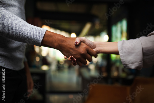 Two multiracial business colleagues working after work or during coffee break in a restaurant. Man and woman shaking hands after successful meeting..